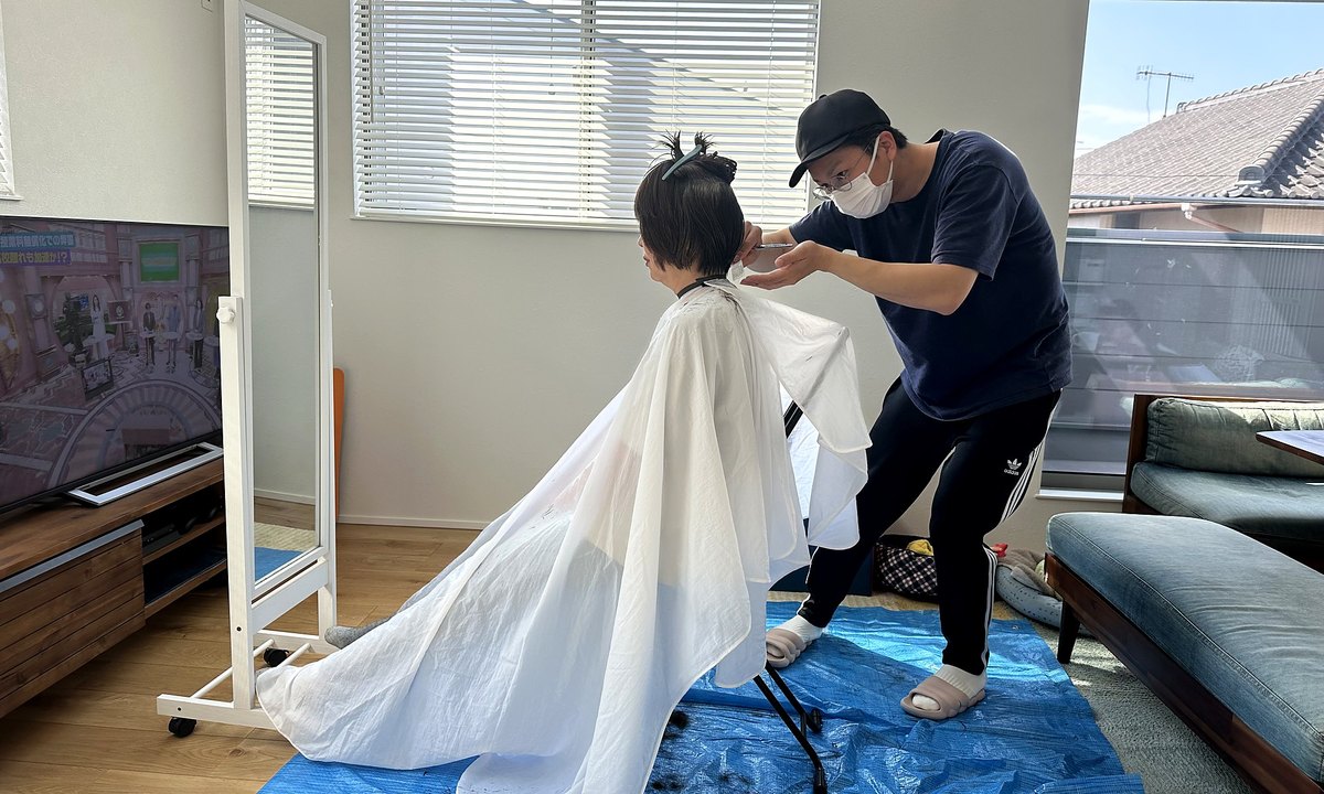 ご自宅のリビングで、ケープをかけてヘアカットをしている様子